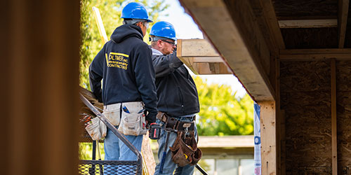 A student and instructor inspect and overhang on a house during construction.
