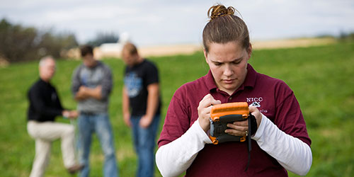 A female NICC student checks a handheld GIS in a field.