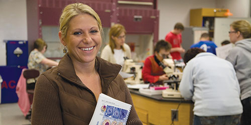 A female student poses in front of a class in the science lab.