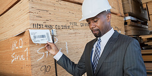 A construction manager checks a delivery tag for a stack of plywood.