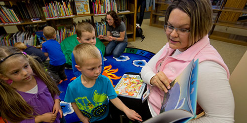 An early childhood instructor reads to children in the library.