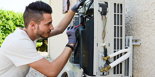 A tech works on an air conditioning unit on a house.