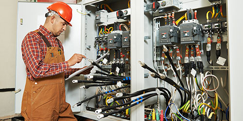 An electrician works on a large power panel in an industrial building.