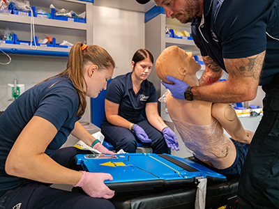 Three Paramedic students work with a mannequin in the lab.