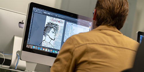 Male graphic design student works at a computer
