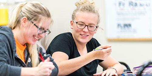 Two female students work on a group project together in the classroom.