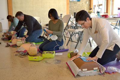 Four students from a local business practicing CPR and AED use during a training session.