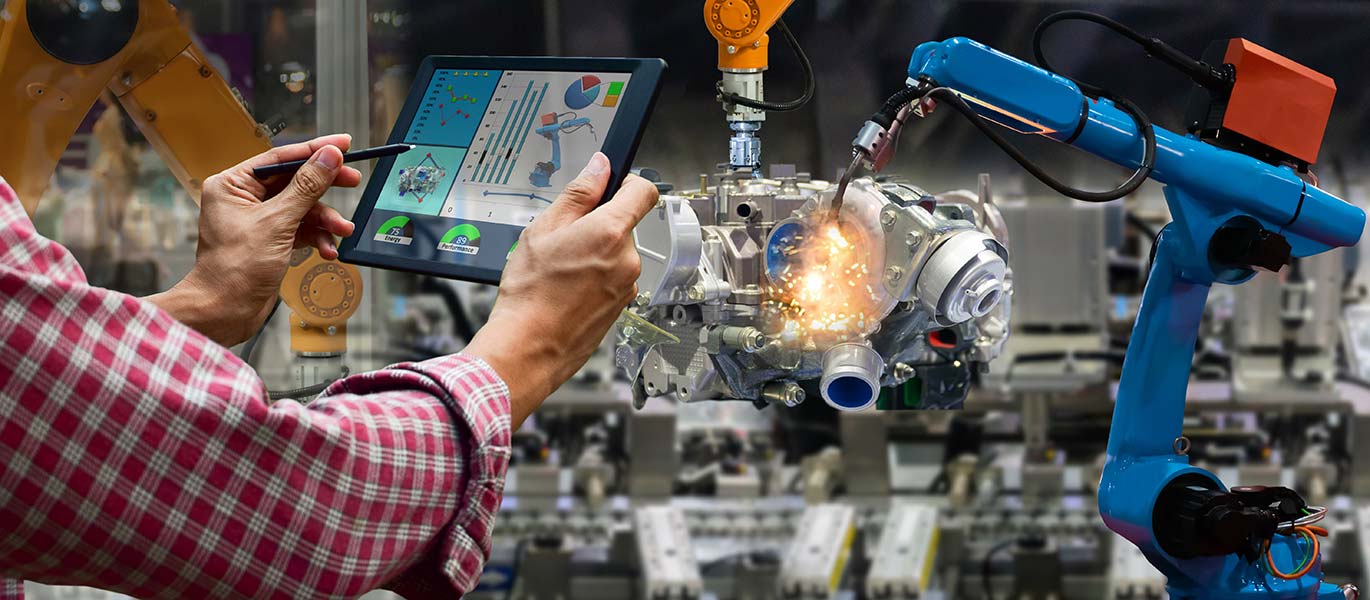 A person controls two manufacturing robots with a tablet.