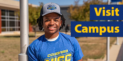 Male student in NICC shirt and hat posing outside at the Peosta campus