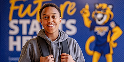 Student posing with backpack in front of the spirit wall
