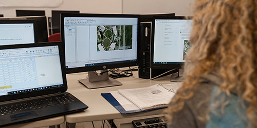 Female student works in front of multiple computer monitors showing Ag yields