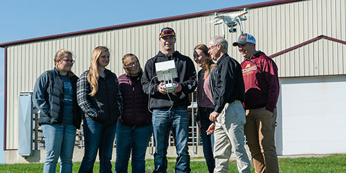 A group of ag students gather outside with a teacher and work with a drone
