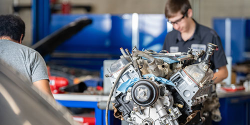 Two male auto tech students rebuild a small engine in the auto lab.