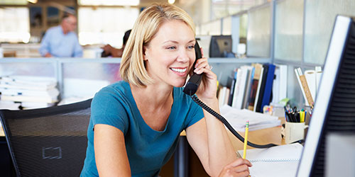 A female office associate answers the phone at her desk.