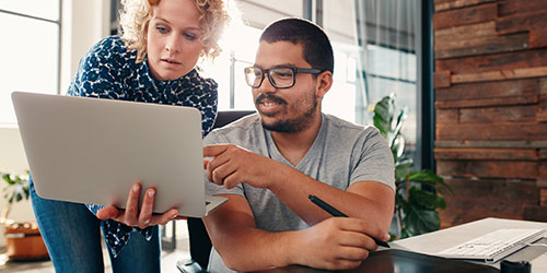 A female office manager and co-worker look at a computer.