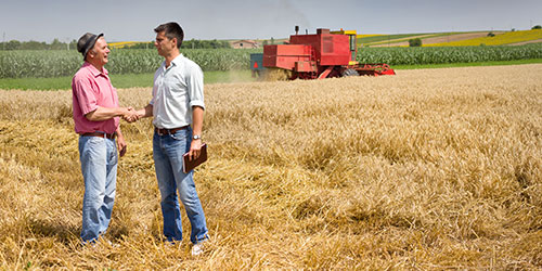 A farmer shakes hands with an agriculture finance officer in a field.