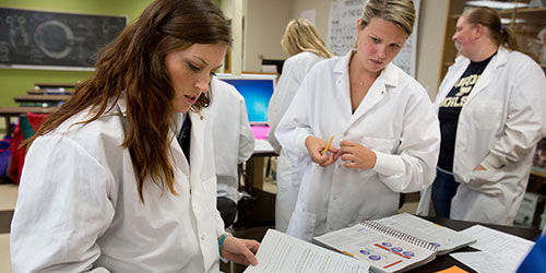 Female students in lab coats in an NICC science lab.