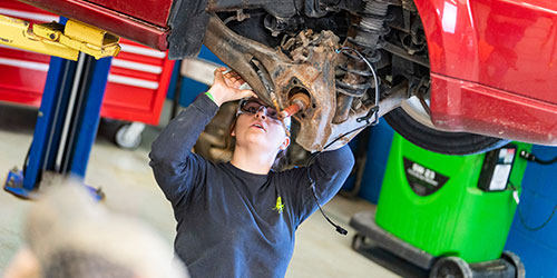 A female auto mechanic student inspects the axle of a car on a lift.