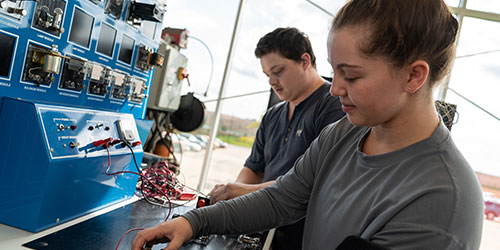 Two industrial maintenance students work on an electrical simulator.