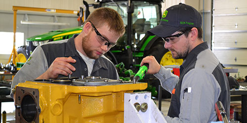 Two John Deere TECH students work on a combine engine.