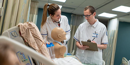 Two nursing students check the temperature of a simulation mannequin in the lab.