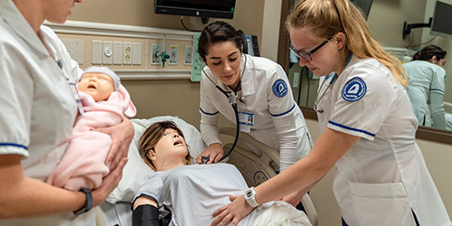 Three female nursing students practice on a mannequin in the health simulation lab.