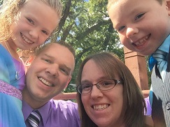 Drew Batterson smiles for photo with wife and two children surrounding him.